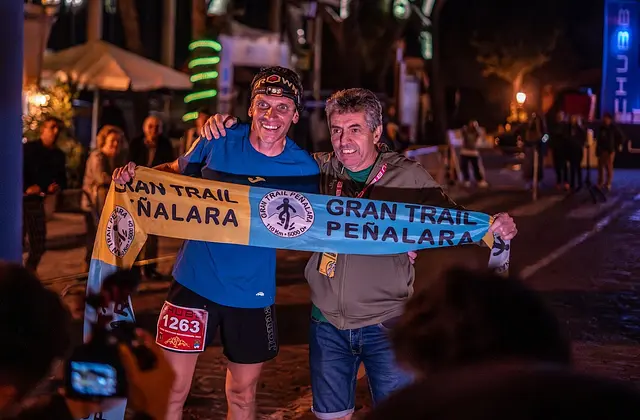 A runner celebrates at the finish in Navacerrada with a Gran Trail Peñalara scarf